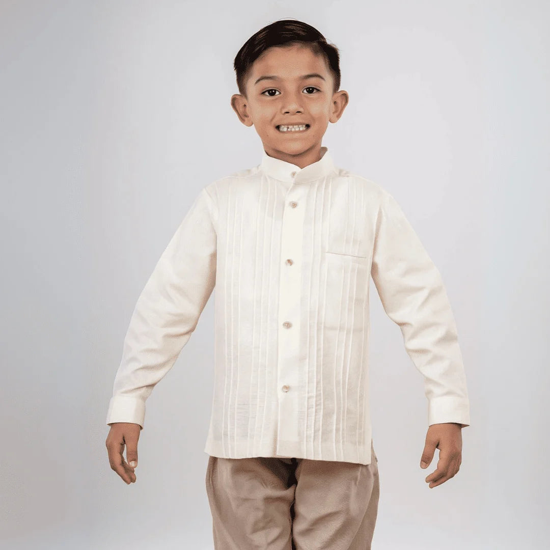 Modelo infantil luciendo una camisa guayabera para niño de manga larga en manta de algodón manta de Guayaberas LeMaan, destacando el cuello mao y las alforzas tradicionales para un estilo elegante y fresco.